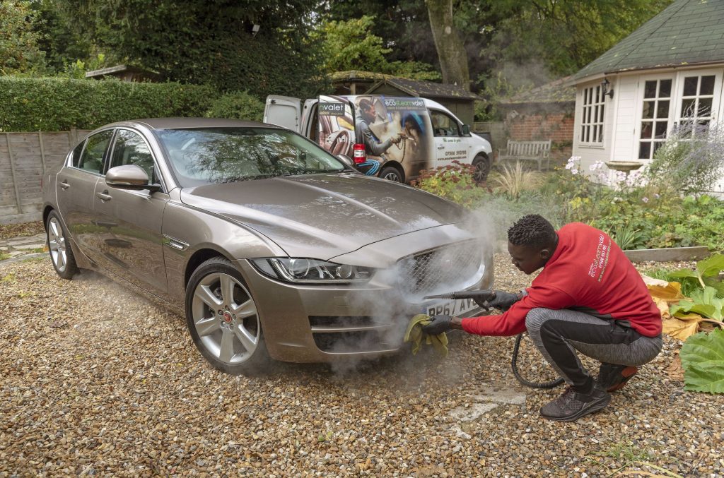 Man steam cleaning a luxury car on a home visiting valet service. 